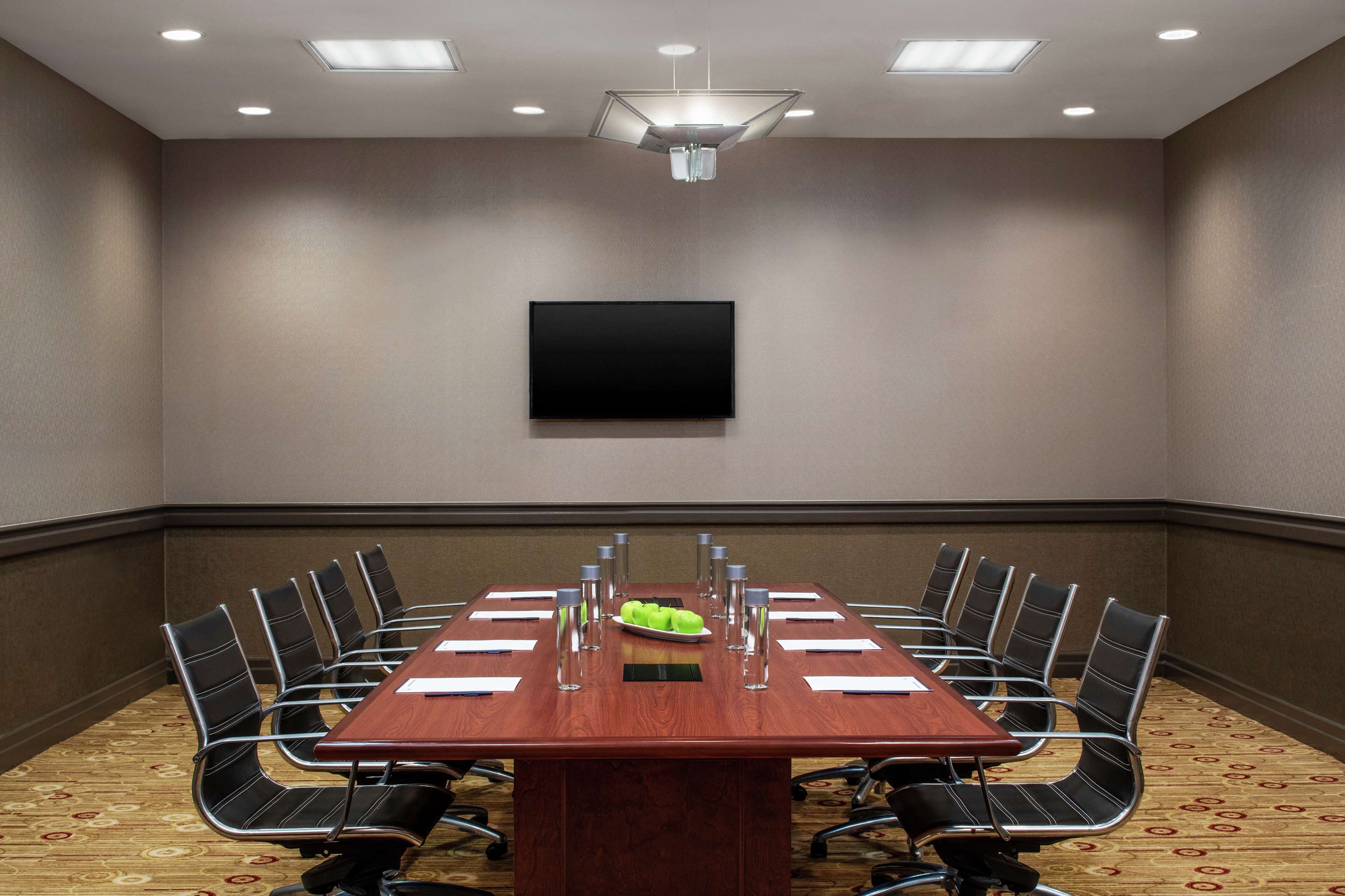 A conference room with a long table, chairs, a flat-screen TV, and a fruit bowl.