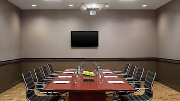 A conference room with a long table, chairs, a flat-screen TV, and a fruit bowl.