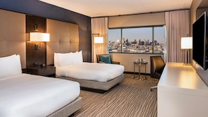 A hotel room with two beds, a city view, a small table, and a TV.