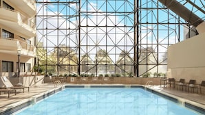 An indoor swimming pool with clear glass walls, sun loungers, and a view of the outside.