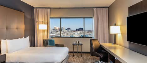 Quarto de hotel com duas camas, uma escrivaninha, uma cadeira, televisão e vista para a cidade.