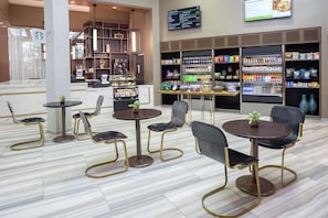 Interior de una cafetería moderna con disposición de mesas, un menú y una variedad de bebidas y aperitivos.