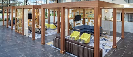 Un lobby moderno e interior con fachada de vidrio, separadores de madera y zonas de estar.