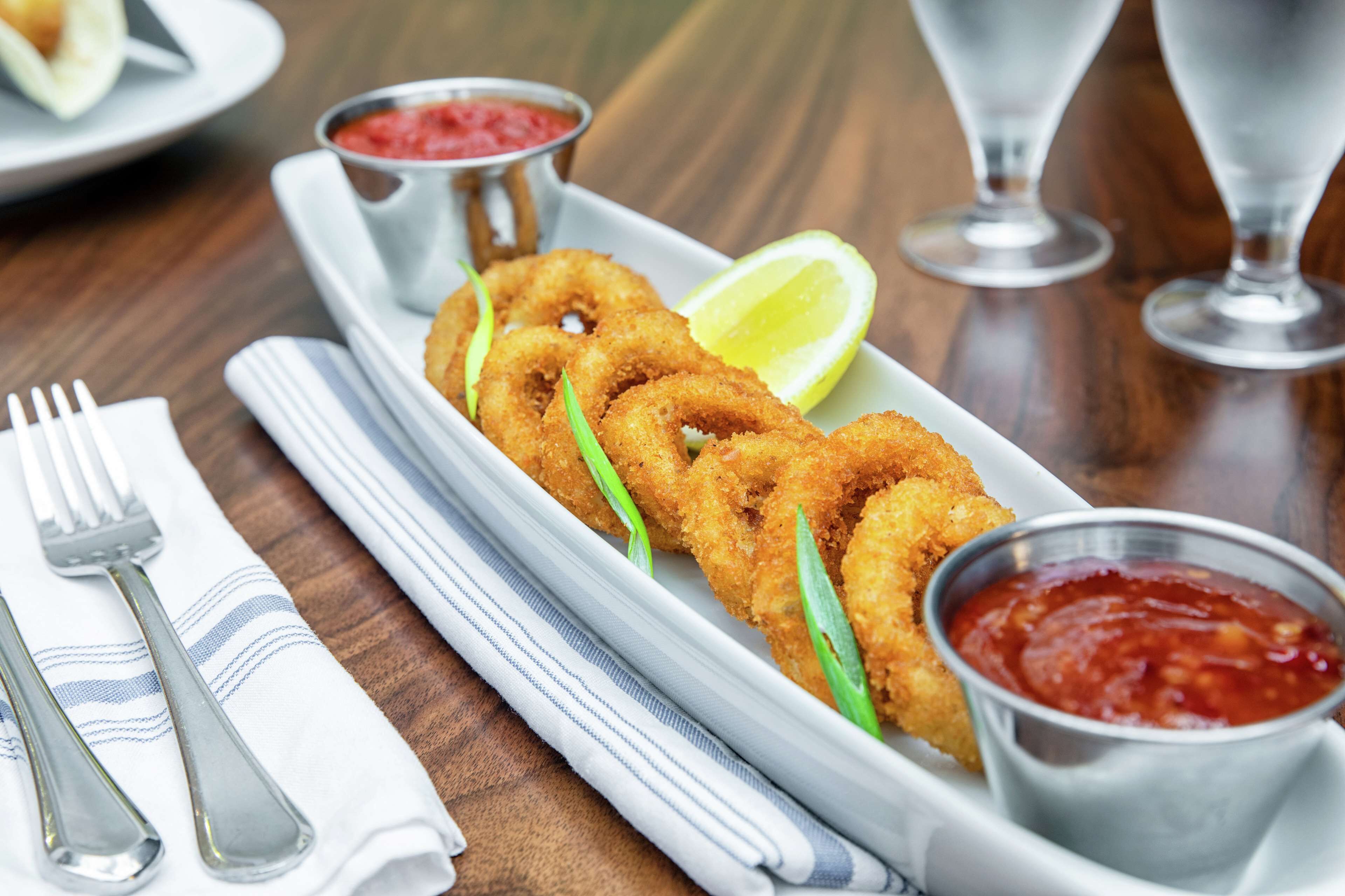 A plate of fried calamari with lemon wedges and two dipping sauces.