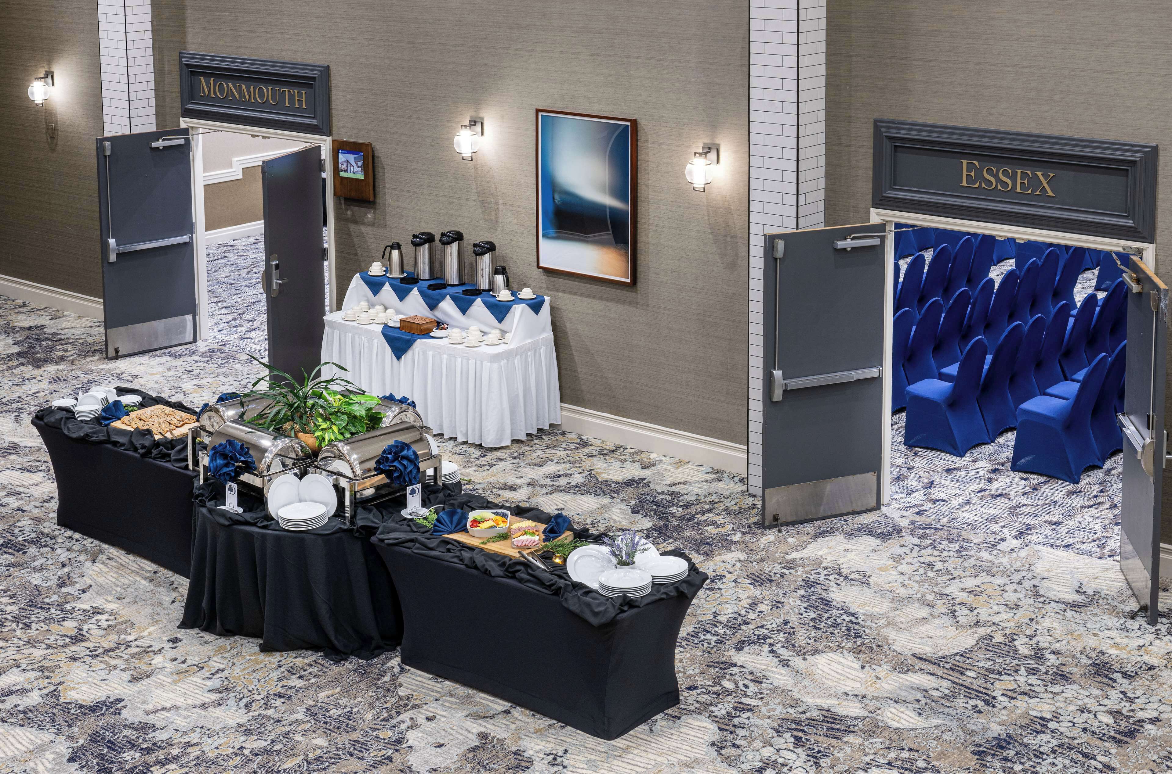 Vestíbulo de hotel con una mesa de buffet, zona de estar y señalización direccional para Monmouth y Essex.