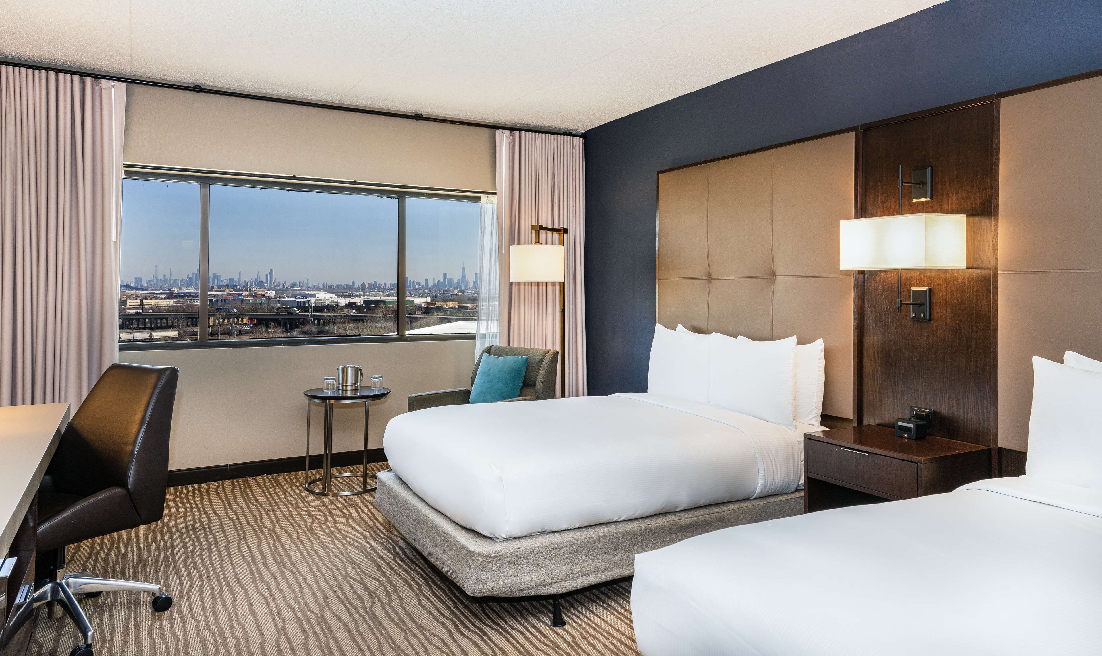 A hotel room with a large window, a bed, a desk, and a chair.