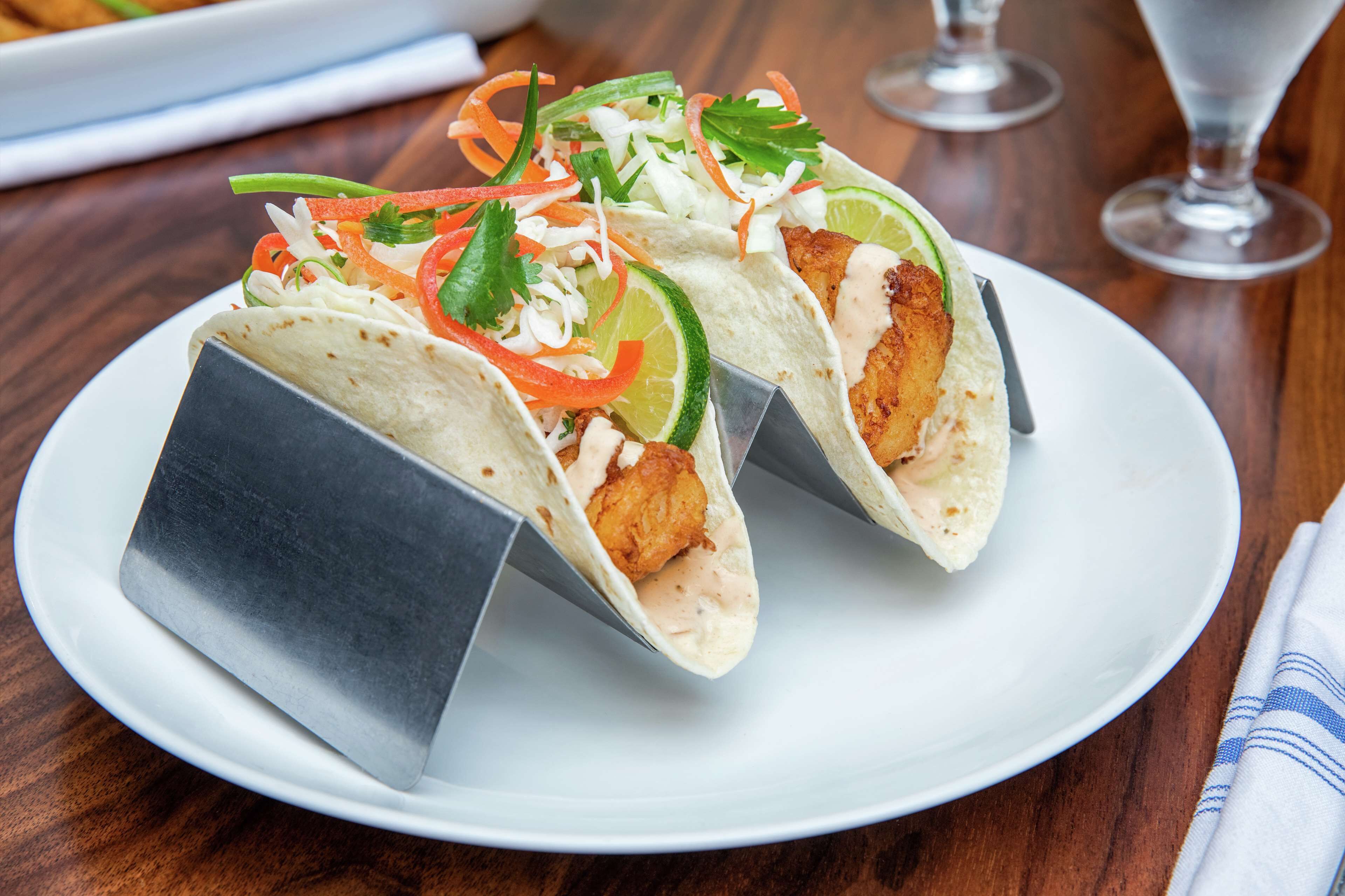 A plate of tacos with lime, carrots, and cilantro on a wooden table.