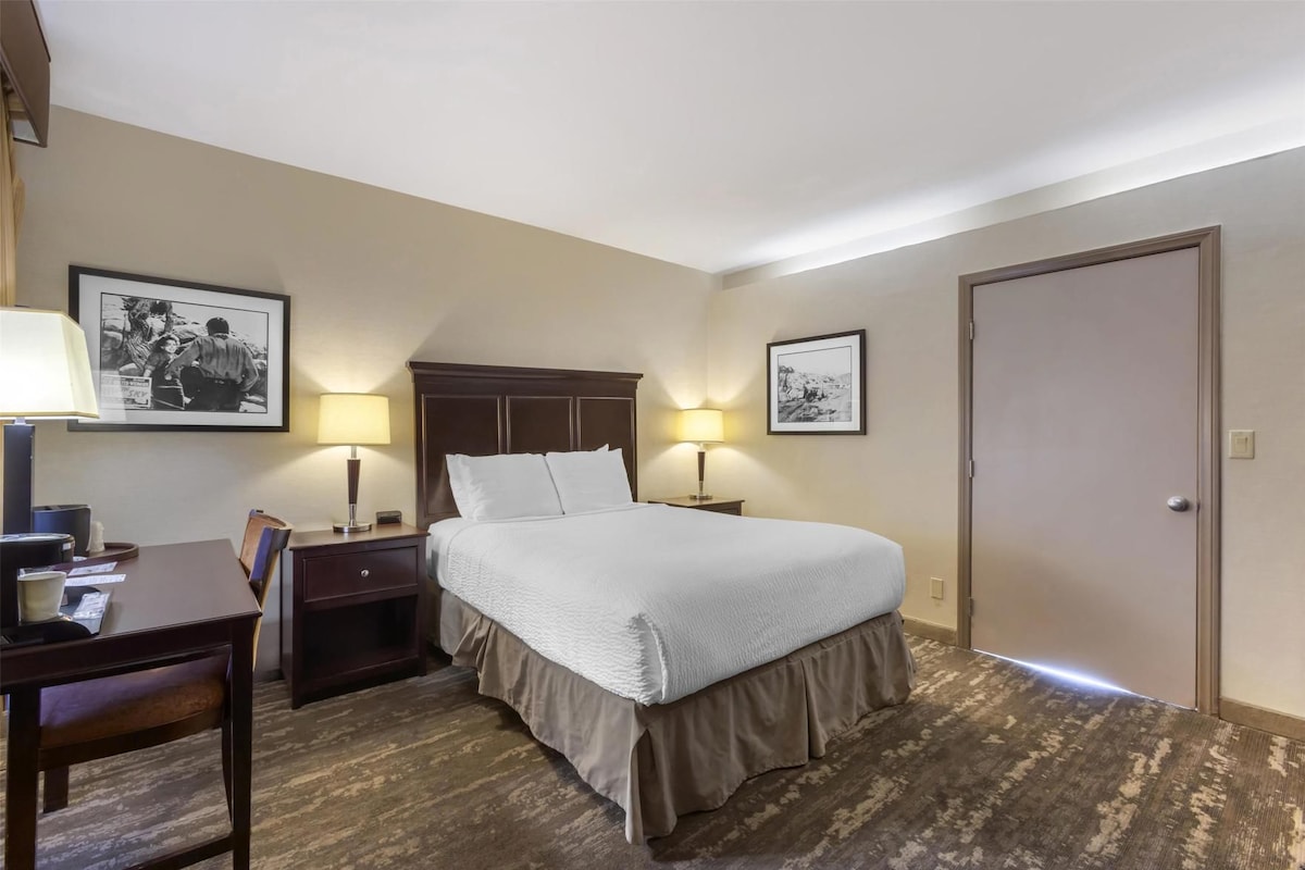 Ein Hotelzimmer mit einem Bett, zwei Nachttischen, einem Schreibtisch mit Stuhl und zwei Wandlampen.