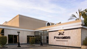A building with a sign reading 'JAZ PYRAMIDS' and a paved entrance area with a lamp post and trimmed bushes.