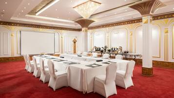 A conference room with a long table, white chairs, a projector screen, and a chandelier.