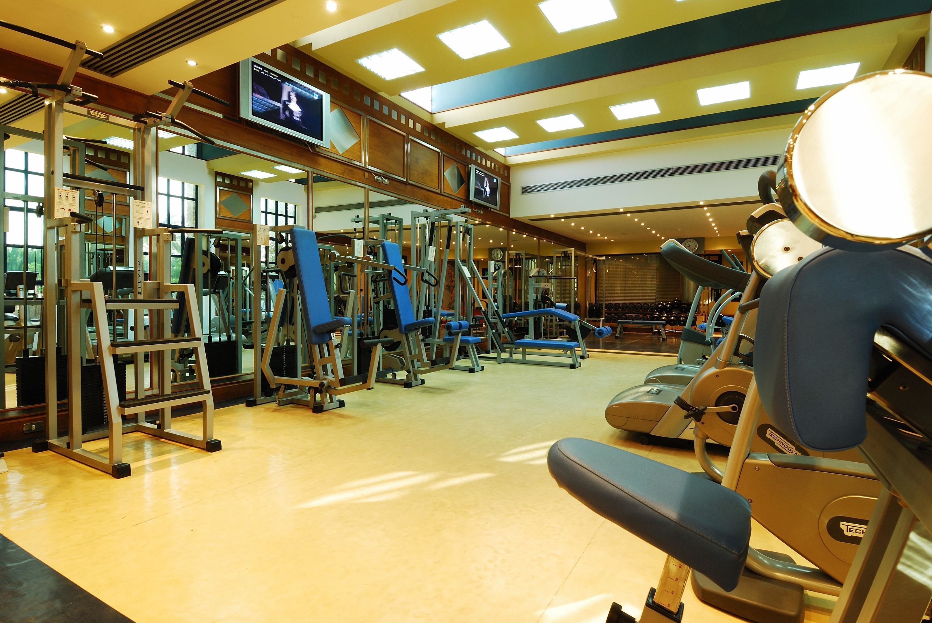 Un gimnasio con equipo de ejercicio, una pantalla de televisión y un muro con espejos.
