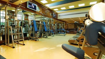 Un gimnasio con equipo de ejercicio, una pantalla de televisión y un muro con espejos.