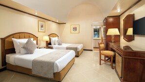A hotel room with two beds, a desk, a chair, and a TV.