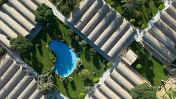 Eine Vogelperspektive zeigt einen Ferienort mit mehreren bungalowsartigen Gebäuden, einem zentral gelegenen Schwimmbecken und gepflegten Gärten.