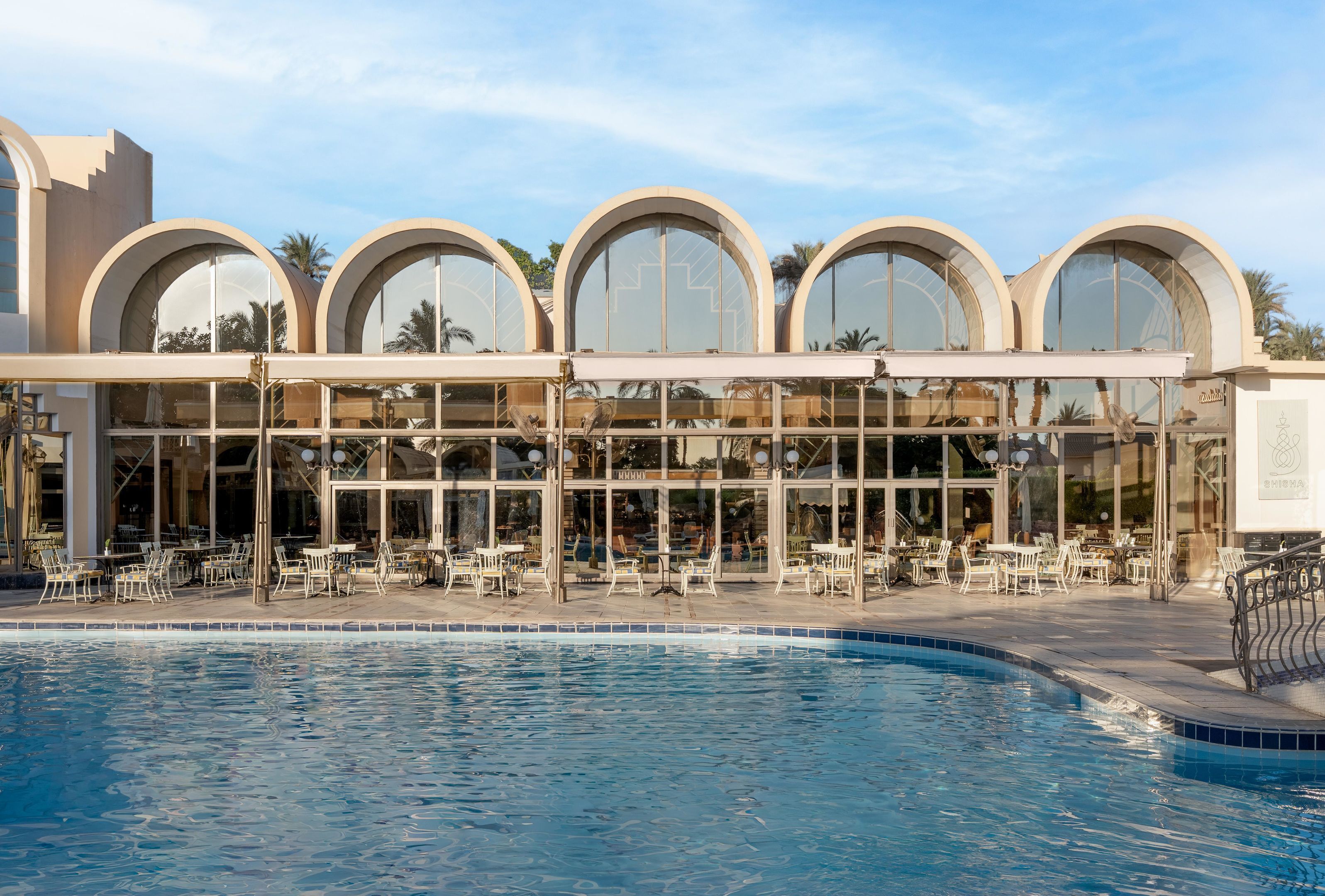 Een hotel met een zwembad, terras en grote, gebogen ramen.