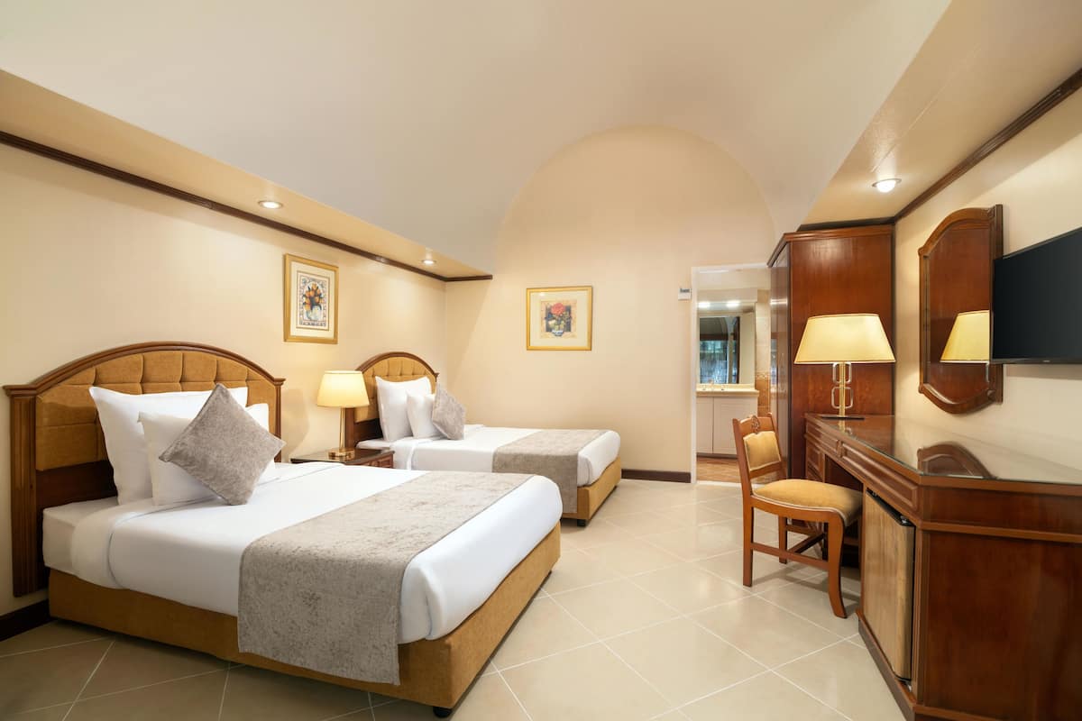 A hotel room with two beds, a desk, a chair, and a TV.