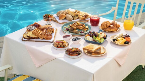 A dining table with a variety of breakfast foods and drinks by a poolside. - JAZ Pyramids Resort (Giza)
