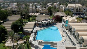 A resort with a large swimming pool, multiple lounge areas, and a view of pyramids in the distance. - JAZ Pyramids Resort (Giza)