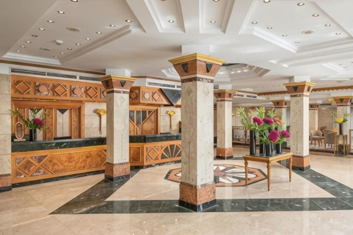 A lobby with marble floors, wooden reception desks, and columns.