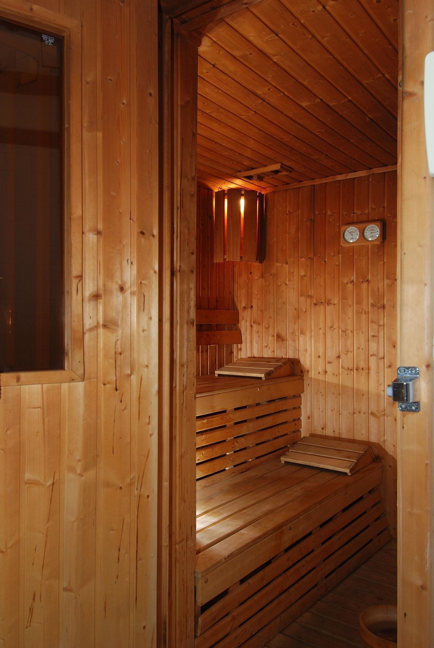 A wooden sauna with benches and a bench seat, wooden walls, and a door with a window.