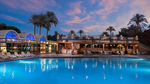 A poolside area with lounge chairs, a bar, and a building with large windows.