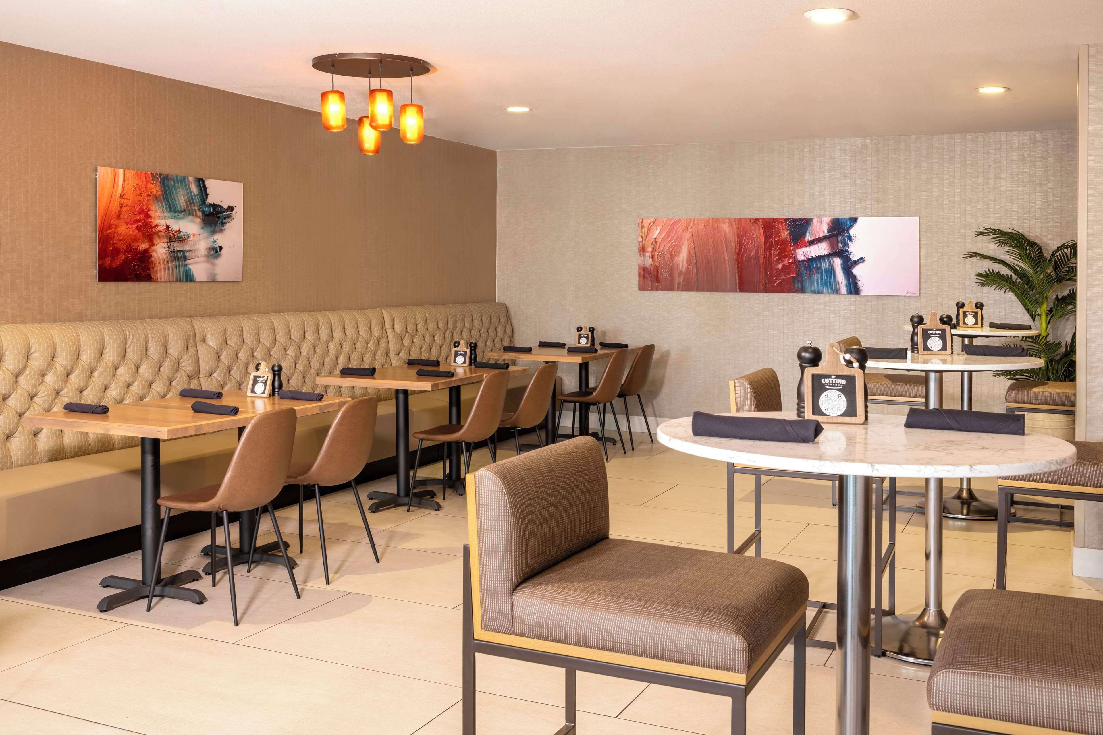 Ein modernes Restaurant mit einer Mischung aus Sitzecken und Tischen, einer gepolsterten Sitzecke und einem runden Tisch mit einer Uhr.