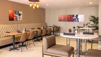 Un restaurant moderne proposant un mélange de banquettes et de tables, avec une banquette capitonnée et une table ronde ornée d’une horloge.