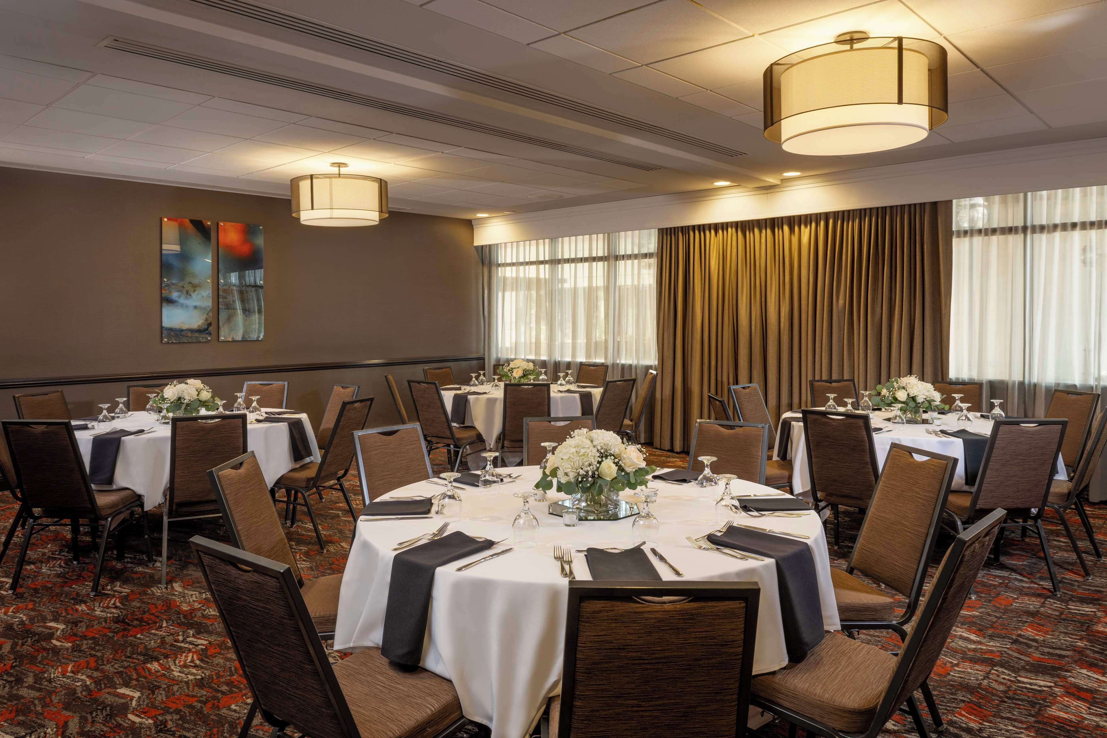 A conference room with round tables, chairs, and a large window with curtains.