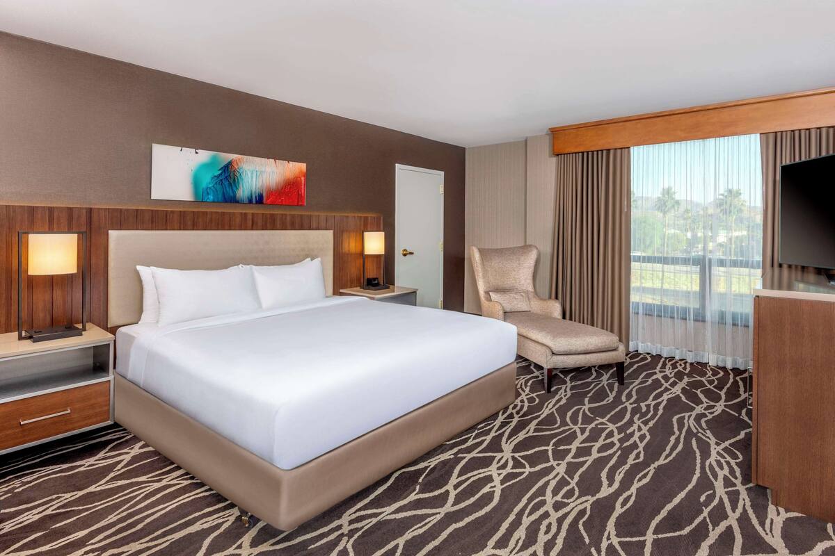 Une chambre d’hôtel avec un grand lit, une chaise, une télévision et une fenêtre avec des rideaux.