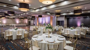 A banquet hall with round tables set for dining, featuring gold chairs and white tablecloths.