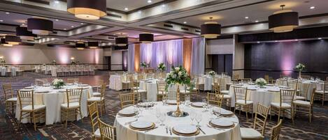 A banquet hall with round tables set for dining, featuring gold chairs and white tablecloths.