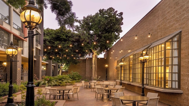 An outdoor patio area with tables and chairs, string lights, and a brick building. - DoubleTree by Hilton Hotel San Bernardino (San Bernardino)