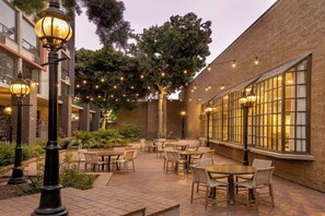 Un'area patio all'aperto con tavoli e sedie, luci a stringa e un edificio in mattoni.