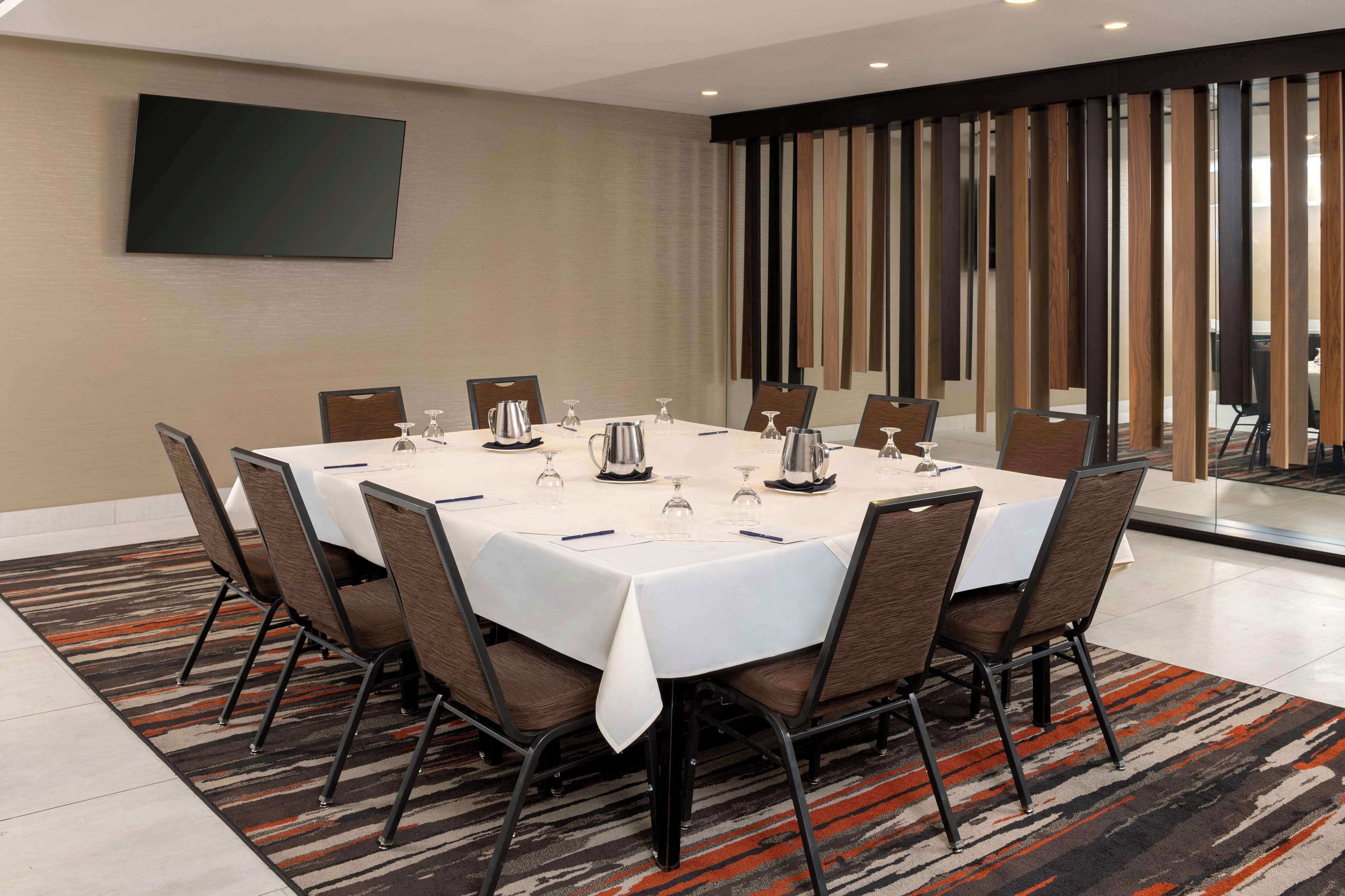 A conference room with a large table, chairs, a TV on the wall, and a patterned carpet.