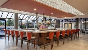 A modern bar area with a long counter, multiple bar stools, and a variety of bottles and glasses. - DoubleTree by Hilton Hotel San Bernardino (San Bernardino)