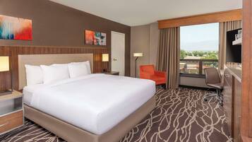 Quarto de hotel com uma cama grande, uma escrivaninha, uma cadeira e vista para a cidade.