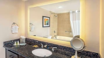 Un baño con encimera de granito, un lavabo, un espejo, toallero y un cuadro en la pared.