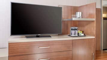 A modern kitchen with a flat-screen TV, wooden cabinets, and a coffee machine.