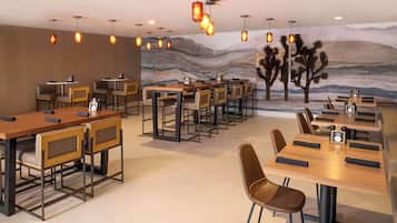 A restaurant with multiple dining tables and chairs, a mural on the wall, and pendant lighting.