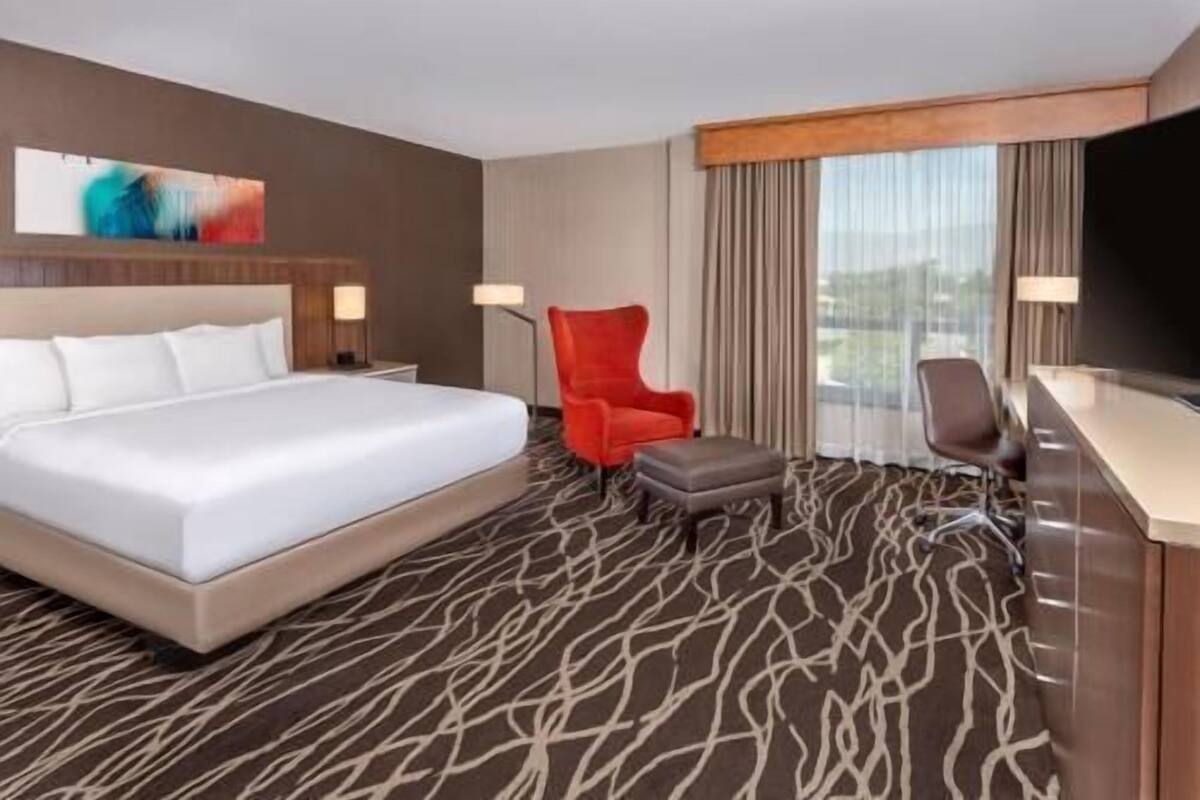 Une chambre d’hôtel avec un grand lit, un fauteuil rouge, un pouf gris, un bureau et une télévision.