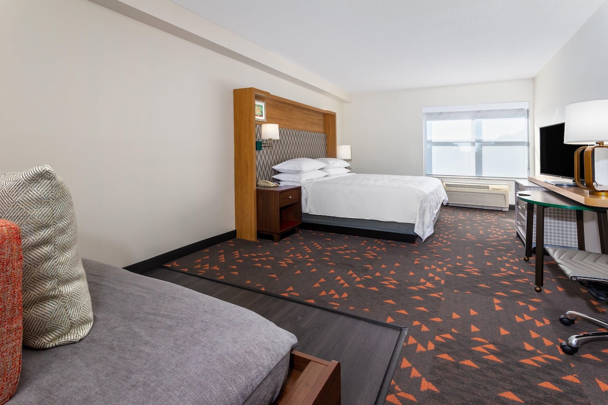 A hotel room with a bed, a desk, a chair, and a large window.