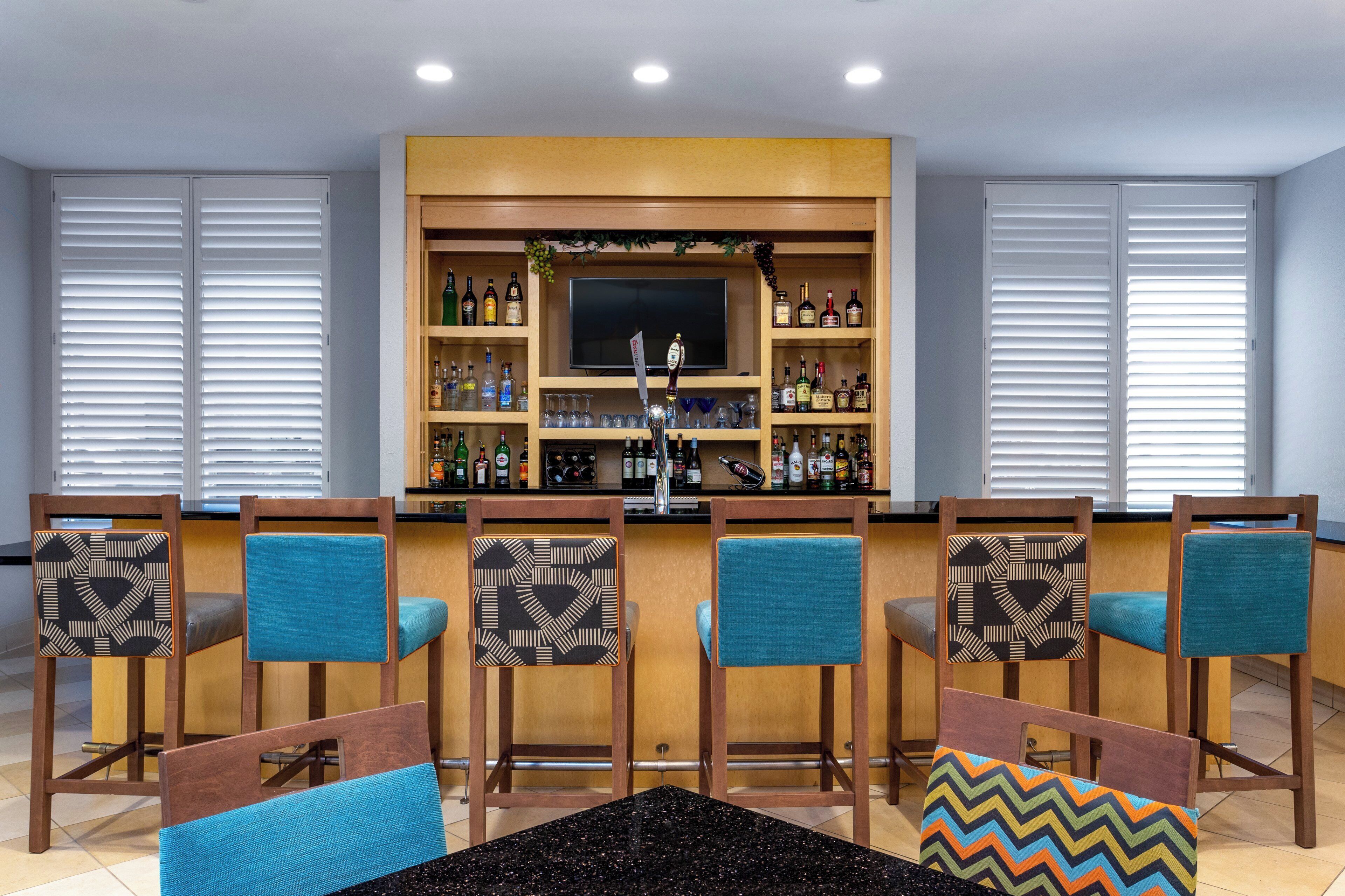 A bar area with a television, shelves of bottles, and bar stools with patterned cushions.