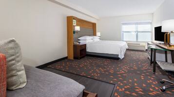 A hotel room with a bed, a desk with a computer, a chair, and a window.