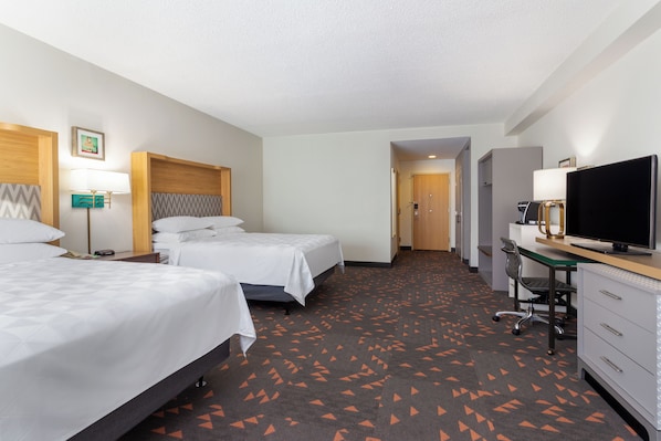 A hotel room with two beds, a desk, a chair, a television, and a desk lamp.