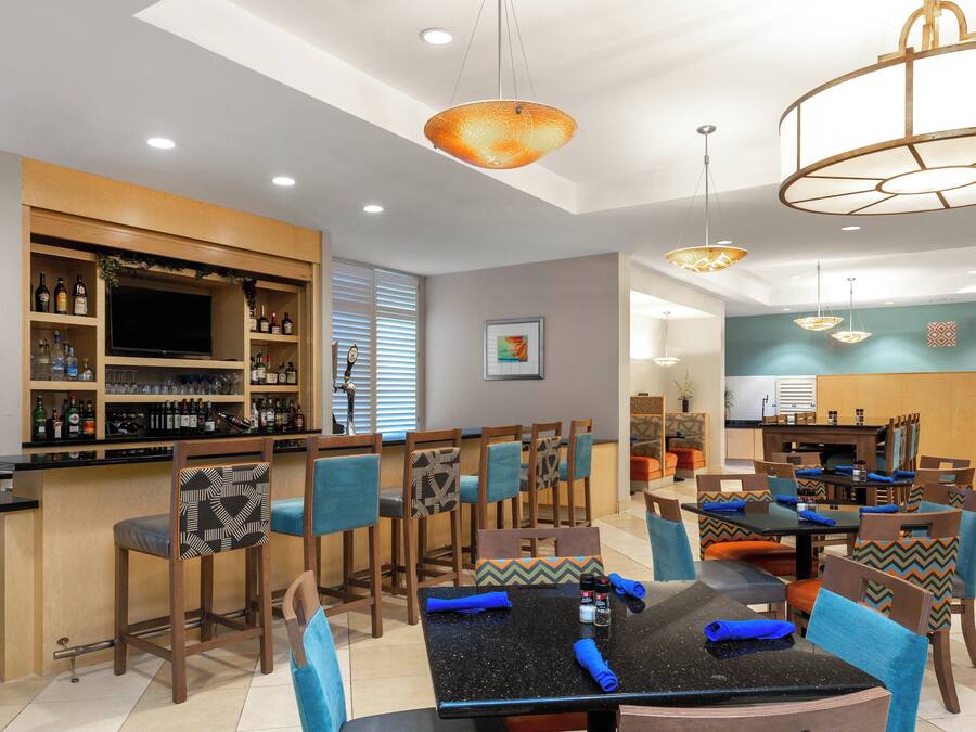 A restaurant with a bar area, multiple dining tables, and chairs with patterned cushions.