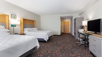 A hotel room with two beds, a desk, a television, and a door leading to another room.