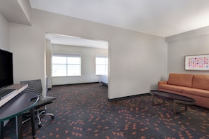A hotel room with a desk, chair, sofa, and a large window.