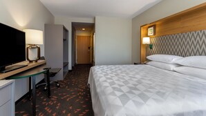 Ein Hotelzimmer mit einem Bett, einem Schreibtisch mit Computer, einem Fernseher und einer Lampe.