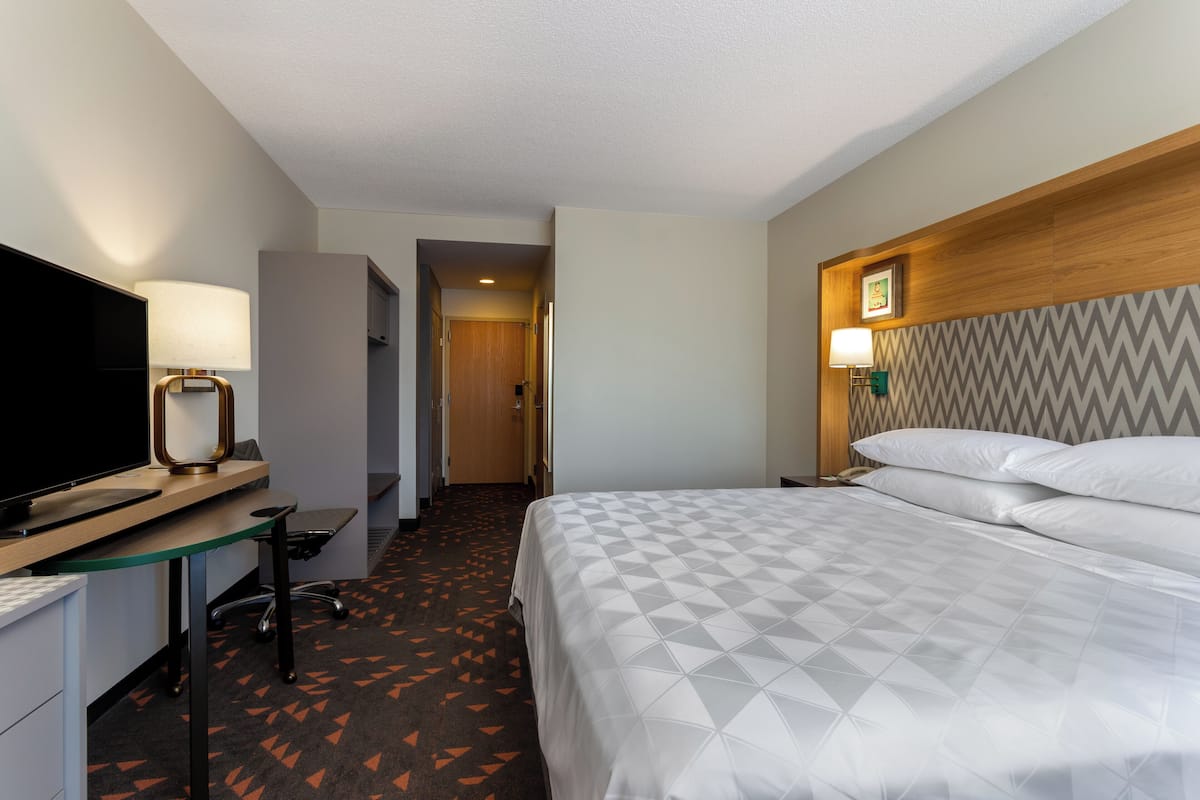 A hotel room with a bed, a desk with a computer, a television, and a lamp.