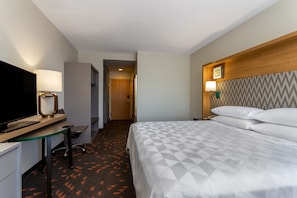 A hotel room with a bed, a desk with a computer, a television, and a lamp.